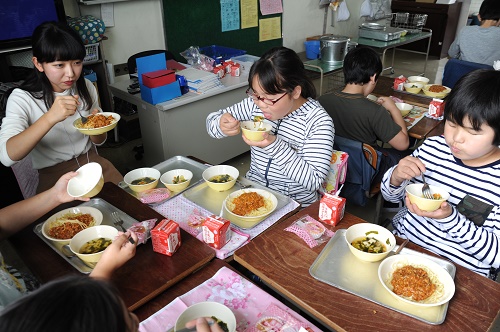 児童と給食を食べる加藤綾夏さん（農学科4年生）「タウンニュース多摩区版」5月11日号掲載記事より