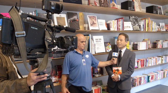 Vice President Masami Kobayashi being interviewed in front of the donated manga books