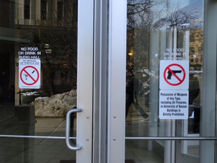 カンザス大学の建物の入り口のサインには、銃の持込み禁止のサインが（向かって左のサインは、「喫煙禁止」）。